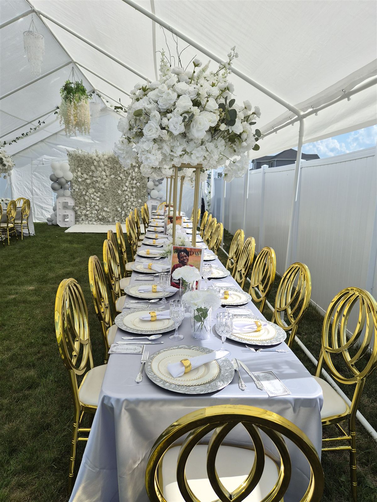 Close-up of a tented table setting with a tall white floral centerpiece, gold ring chairs, and ornate silver charger plates